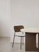 A Co Dining Chair with dark wood back, grey upholstered seat, and black frame next to a round table with a stone top.