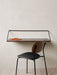 The Co Dining Chair with a black upholstered seat and dark wood back, set at a wall-mounted desk in a minimalist room.