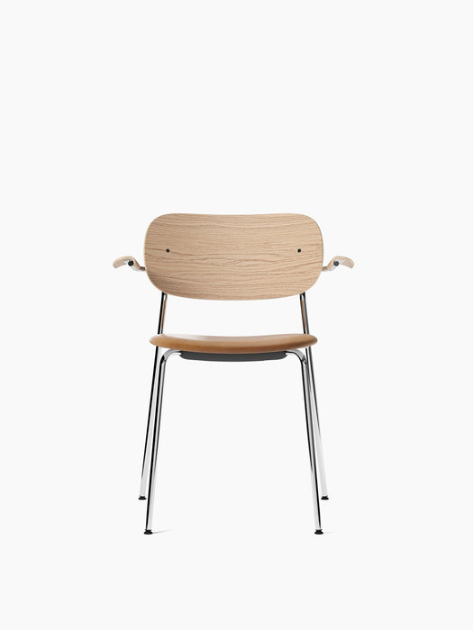 Front view of the Co Dining Chair with armrests, with a natural oak backrest, tan Dakar leather seat, and chrome frame.