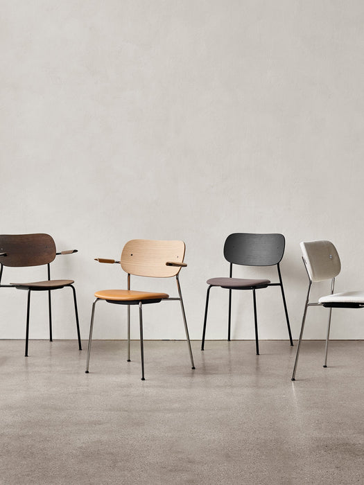 A lineup of four Co Dining Chairs in various finishes and upholstery options, both with and without armrests, against a wall.