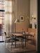 A sunlit dining room featuring several Co Dining Chairs with armrests in various upholsteries around a large black table.