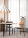 A dining scene featuring the Co Dining Chair with armrests and upholstered seat at a table beneath a large pendant lamp.