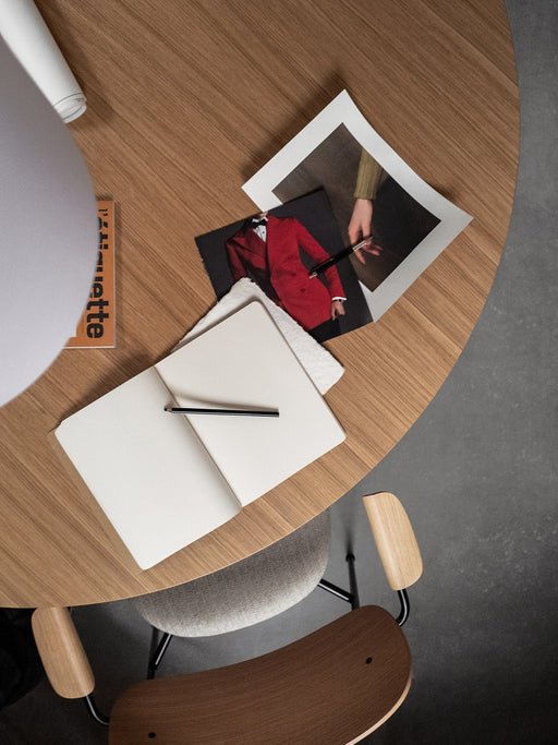 Top-down view of the wooden Androgyne Dining Table with a Co Dining Chair. On the table are a notebook, pencil, and photos.