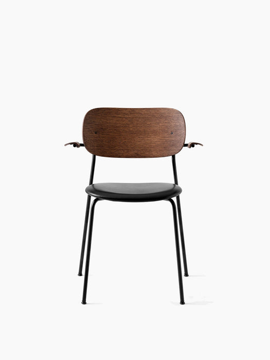 Front view of the Co Dining Chair with armrests. Black steel frame, black upholstered seat, and a smoked oak backrest.