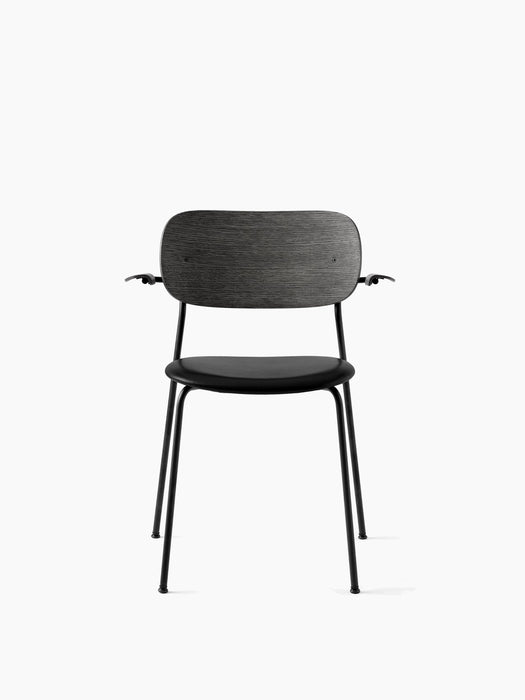 Front view of the black Co Dining Chair with armrests, a black oak backrest, an upholstered seat and a slim metal frame.