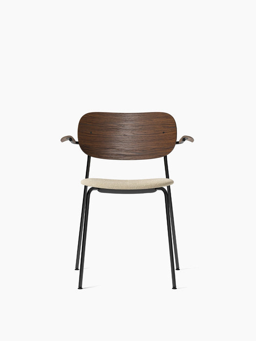 Front view of the Co Dining Chair with armrests, featuring a dark stained oak backrest, light bouclé seat, and black frame.