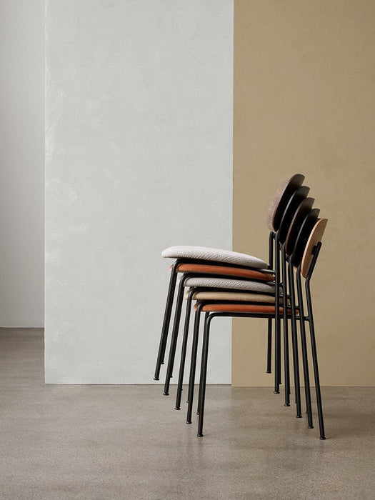 A side view of five Co Dining Chairs stacked in various upholstery and wood veneer finishes against a two-tone wall.