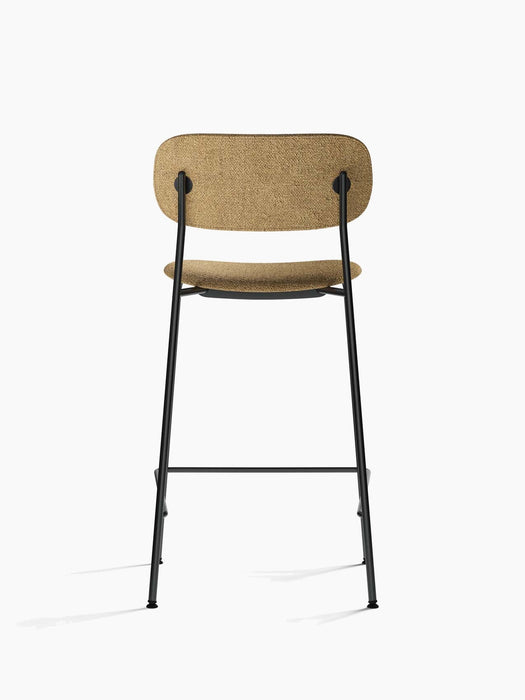 A rear view of the Co Counter Chair, upholstered in textured, light brown bouclé fabric, set on a slender, black steel frame.