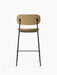 A rear view of the Co Counter Chair, upholstered in textured, light brown bouclé fabric, set on a slender, black steel frame.