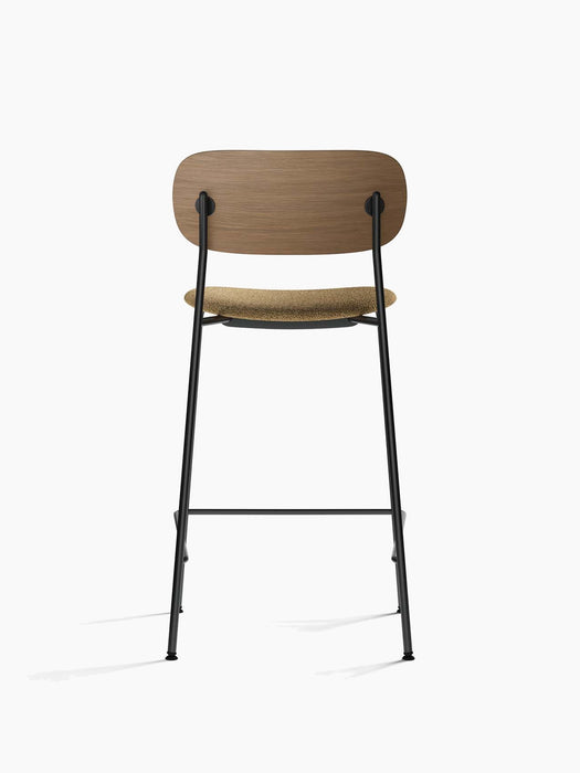 The Co Counter Chair, shown from the back, features a dark stained oak backrest, brown bouclé seat, and black steel frame.
