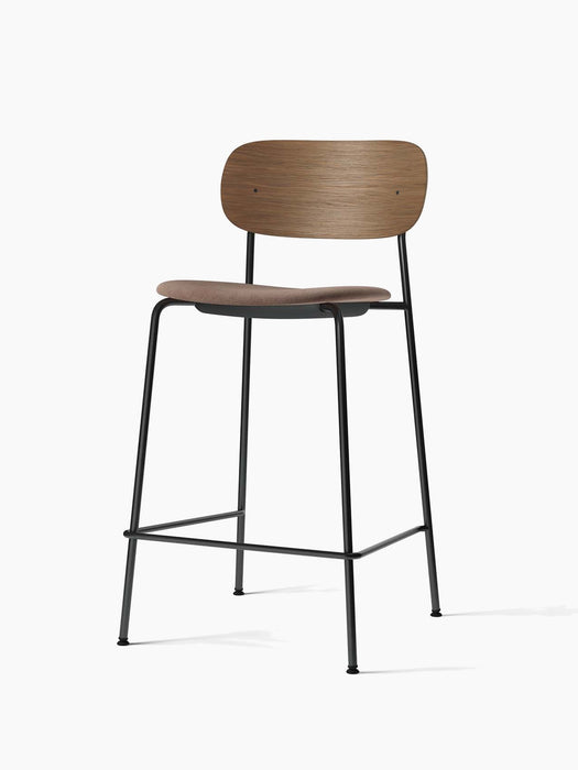 A Co Counter Chair with a black steel frame, a brown upholstered seat, and a contoured backrest in dark stained oak.