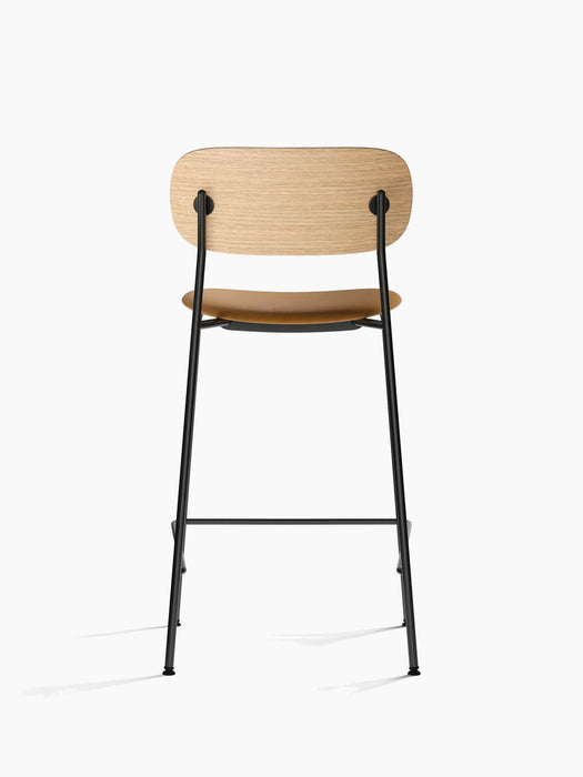Back view of the Co Counter Chair with a natural oak backrest, a tan upholstered seat, and a slender black steel frame.