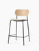 A Co Counter Chair with an upholstered seat, shown at an angle. It has a natural oak backrest and slender black steel frame.