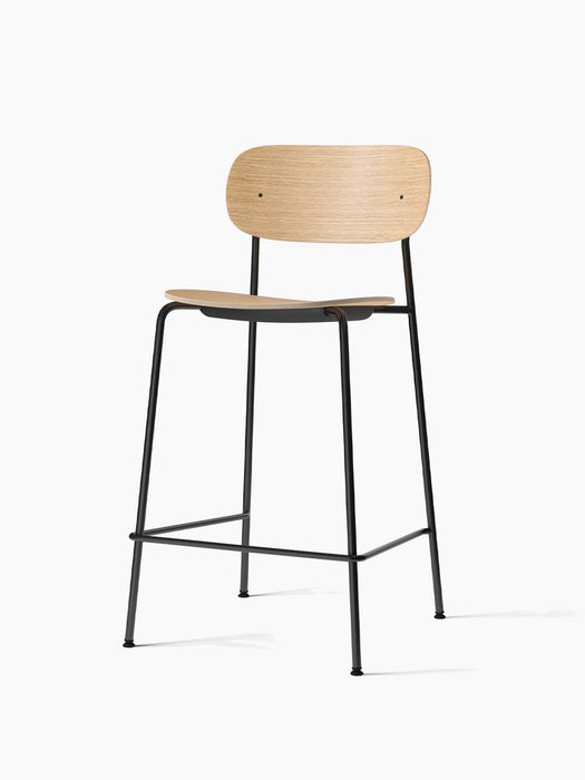 Angled view of the Co Counter Chair, Veneer. It has a natural oak veneer seat and backrest on a slender, black steel frame.