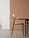 Side profile of the Co Dining Chair with armrest in natural oak veneer, against a minimalist white and terracotta background.