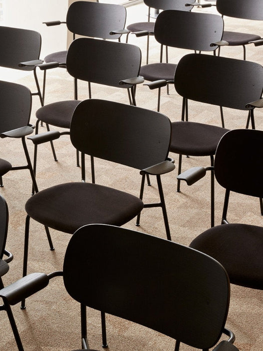 A high-angle view of multiple black Co Dining Chairs with armrests arranged in neat rows on a beige carpeted floor.