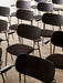 A high-angle view of multiple black Co Dining Chairs with armrests arranged in neat rows on a beige carpeted floor.