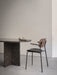 A Co Dining Chair with armrests, featuring a dark wood veneer back and a black seat, sits next to a dark marble dining table.