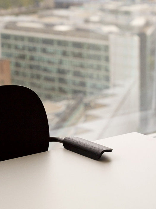 Detailed view of the black Co Dining Chair's armrest on a white table, with a blurred cityscape through a window.
