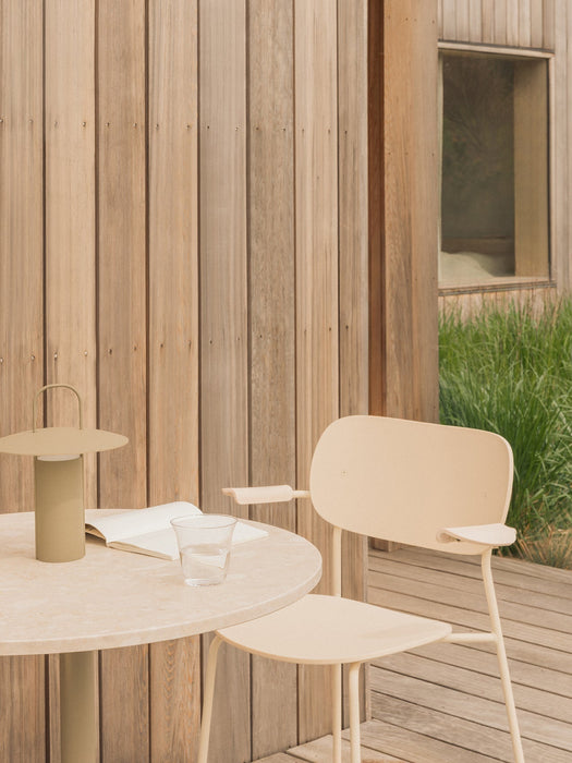 An Ivory Co Dining Chair, Outdoor sits on a wooden deck next to a Nook Dining Table with a Ray Table Lamp and a book on top.