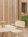 An Ivory Co Dining Chair, Outdoor sits on a wooden deck next to a Nook Dining Table with a Ray Table Lamp and a book on top.
