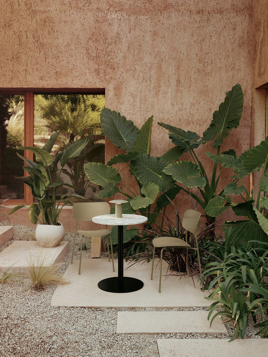 Outdoor patio with two olive Co Dining Chairs, a Harbour Column Table, and a Ray Table Lamp, surrounded by lush green plants.