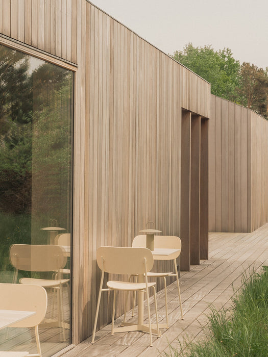 Two ivory Co Dining Chairs, Outdoor and a Nook Dining Table with a Ray Table Lamp on a wooden deck beside a modern building.