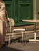 A person in a beige dress stands next to an ivory Co Dining Chair, Outdoor and Nook Dining Table with a Column Portable Lamp.