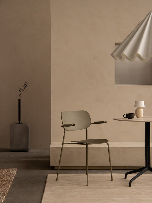 An olive green Co Dining Chair, Outdoor with armrests in a beige room with a Torso Table Lamp and Stance Vase.