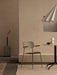An olive green Co Dining Chair, Outdoor with armrests in a beige room with a Torso Table Lamp and Stance Vase.