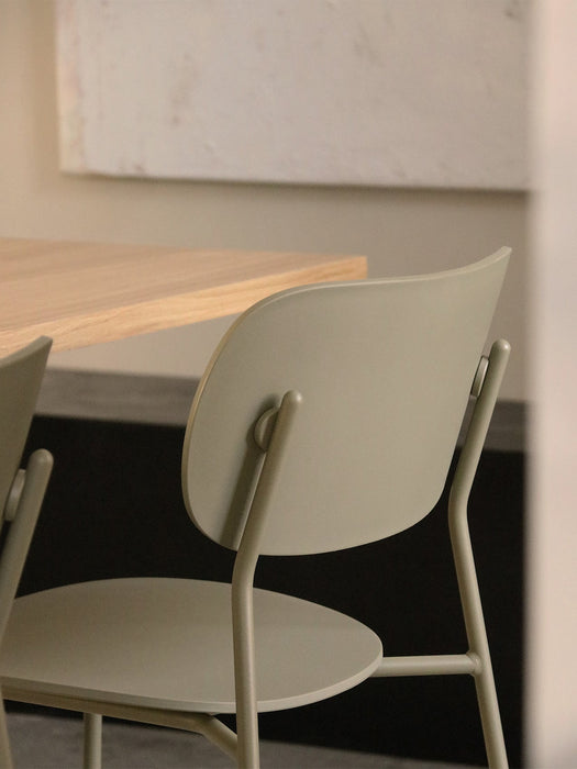 A close-up shot of the back of the olive-coloured Co Dining Chair, Outdoor, positioned next to a light wood dining table.