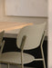 A close-up shot of the back of the olive-coloured Co Dining Chair, Outdoor, positioned next to a light wood dining table.