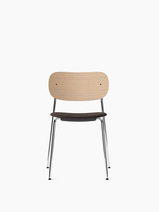 A front view of the Co Dining Chair, featuring a natural oak backrest, a dark upholstered seat, and a slender chrome frame.