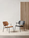 Two Co Lounge Chairs, one in natural oak with a tan seat and one in black, placed on a light rug before a slatted wood panel.
