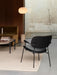 The Co Lounge Chair in black, seen from behind, in a minimalist living room with sofa, coffee table, and glowing floor lamp.