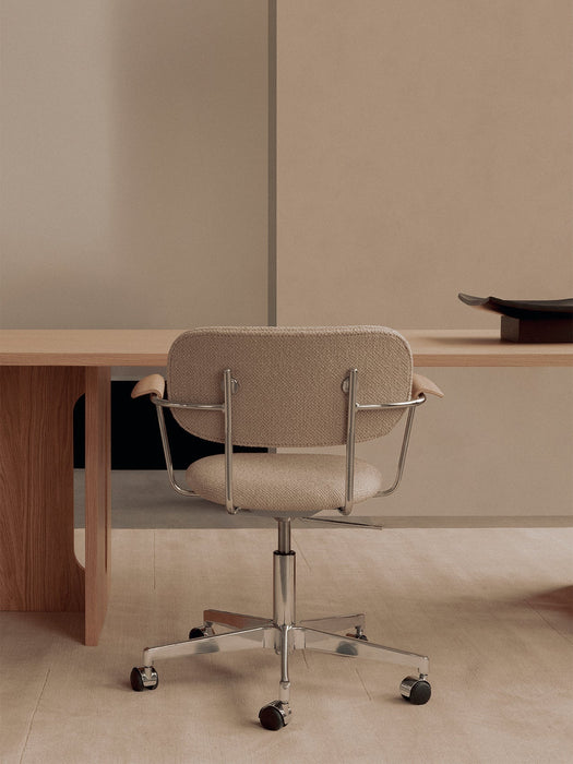 Back view of a Co Task Chair with beige upholstery and a chrome base, positioned at a light oak Androgyne Dining Table.
