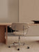 Back view of a Co Task Chair with beige upholstery and a chrome base, positioned at a light oak Androgyne Dining Table.