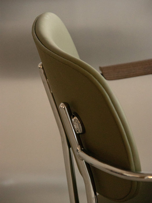 Close-up on the back of the Co Task Chair, detailing the olive green upholstery and polished aluminium frame with armrest.