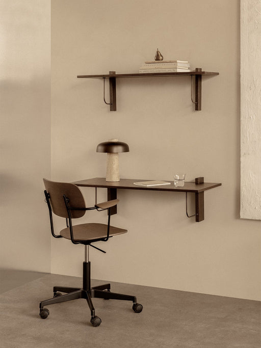 A Co Task Chair at a dark wood Corbel Desk with a Reverse Table Lamp. Above, a Corbel Shelf holds books and a pear.