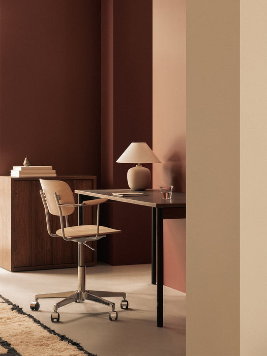 The Co Task Chair in light oak veneer sits at a dark desk with a Torso Table Lamp in a warm, brown-toned office setting.