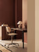 The Co Task Chair in light oak veneer sits at a dark desk with a Torso Table Lamp in a warm, brown-toned office setting.