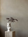 The sculptural white Collapse Vase holding a dark-leafed branch, styled on a square marble Plinth Pedestal.