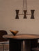 The brass and dark metal Collector Chandelier, 3 hangs over a dark wood Androgyne Dining Table with a decorative brass bowl.