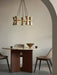 A Collector Chandelier, 5 hanging above a round Androgyne Dining Table set with a Taper Bowl in a room with a beige archway.
