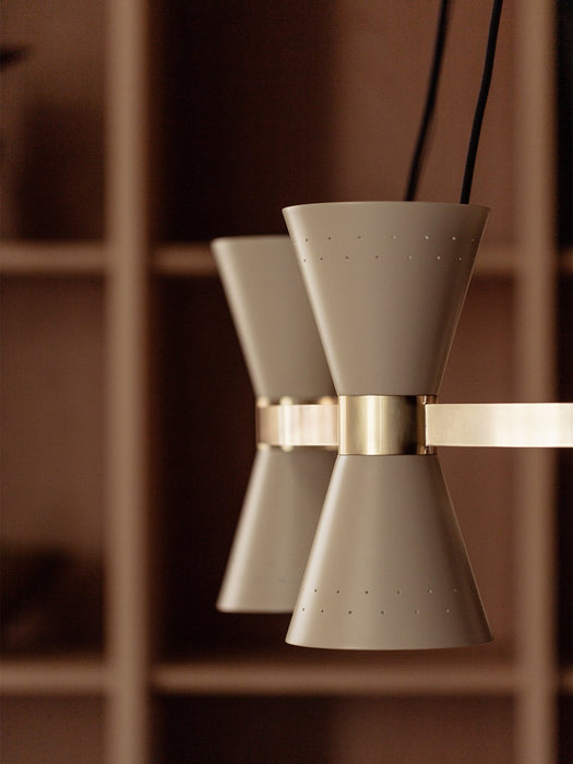 Close-up of the Collector Chandelier, 5, with cream-coloured, perforated hourglass shades on a polished brass arm.