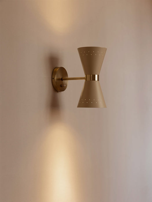 The Collector Wall Lamp in cream with polished brass details, mounted on a pale wall and casting a warm glow up and down.