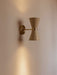 The Collector Wall Lamp in cream with polished brass details, mounted on a pale wall and casting a warm glow up and down.