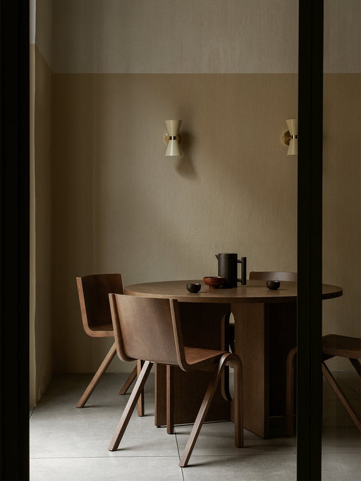 A minimalist dining room with two Collector Wall Lamps on a beige wall above a round wooden table with chairs and a teapot.