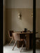 A minimalist dining room with two Collector Wall Lamps on a beige wall above a round wooden table with chairs and a teapot.
