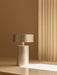 A close-up of the Column Table Lamp in brushed aluminium, sitting on a pale surface with a beam of light in a warm setting.